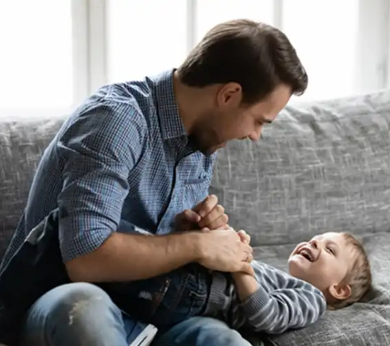 Father laughing and playing with his young child on a couch